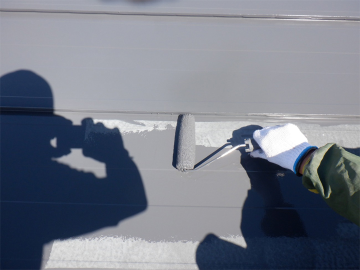 汚れを落とし日光で乾燥させた屋根に塗料をローラーで丁寧に薄く塗っていきます。<br />
カラーは工事前と同じグレーカラーを使用し塗り広げます。 