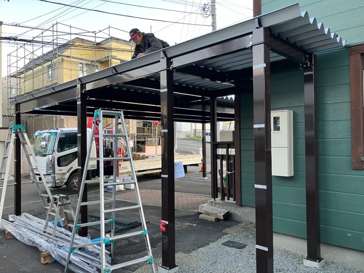 既存の庭部分を整理し、駐車スペースとして活用できるよう地面を整えていきます。あわせて、これまで使用していた1台用カーポートを撤去し、新しいカーポートを設置するためのスペースを確保しました。 その後、特別注文の鉄骨3台用カーポート「AP760L型」を設置していきます。柱や梁を組み上げながらカーポート全体を施工し、3台分の車を駐車できる屋根付きスペースを整えました。 カーポートの設置にあわせて、敷地境界には既存と同様にアルミフェンスを設置しています。庭だった部分まで駐車スペースとして活用できるよう、外構全体を整えていきました。